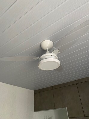 A ceiling fan with a light fixture in a room with a tiled floor and a partial view of a wall.