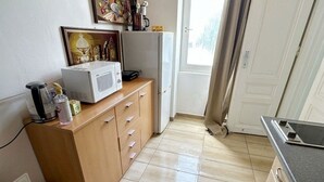 A small kitchenette with a microwave, a refrigerator, a wooden cabinet, and a window with curtains. - Cozy Studio for 4 Near Floridsdorf (Vienna)