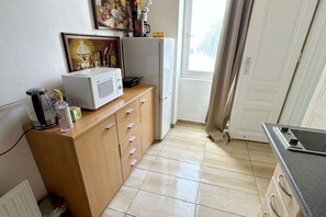 Ett litet pentry med mikrovågsugn, kylskåp, ett träskåp och ett fönster med gardiner.