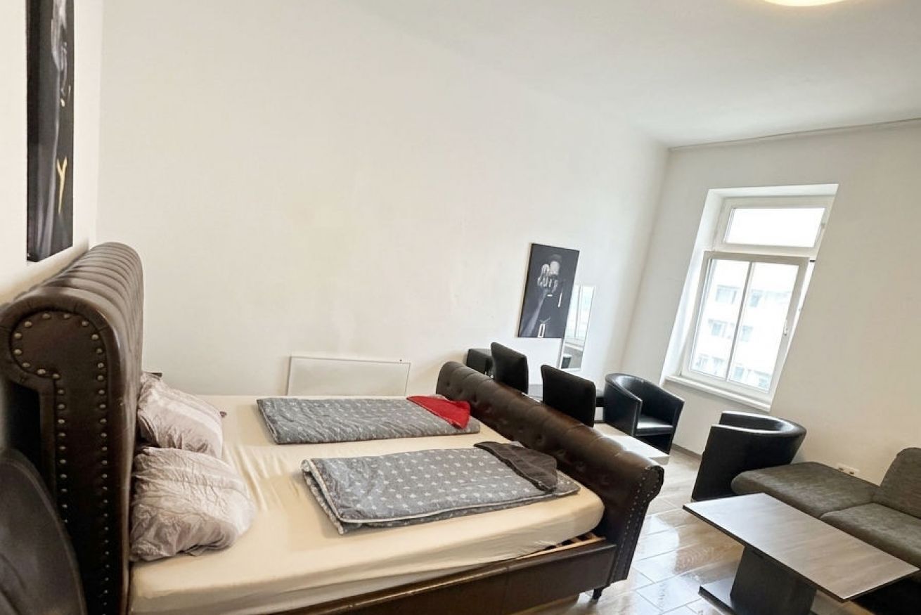 A room with a bed, two chairs, a sofa, and a window.