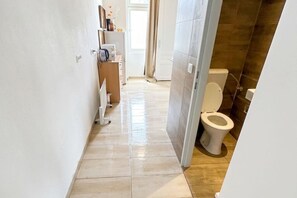 En smal hall som leder till ett badrum med toalett och en duschhörna.