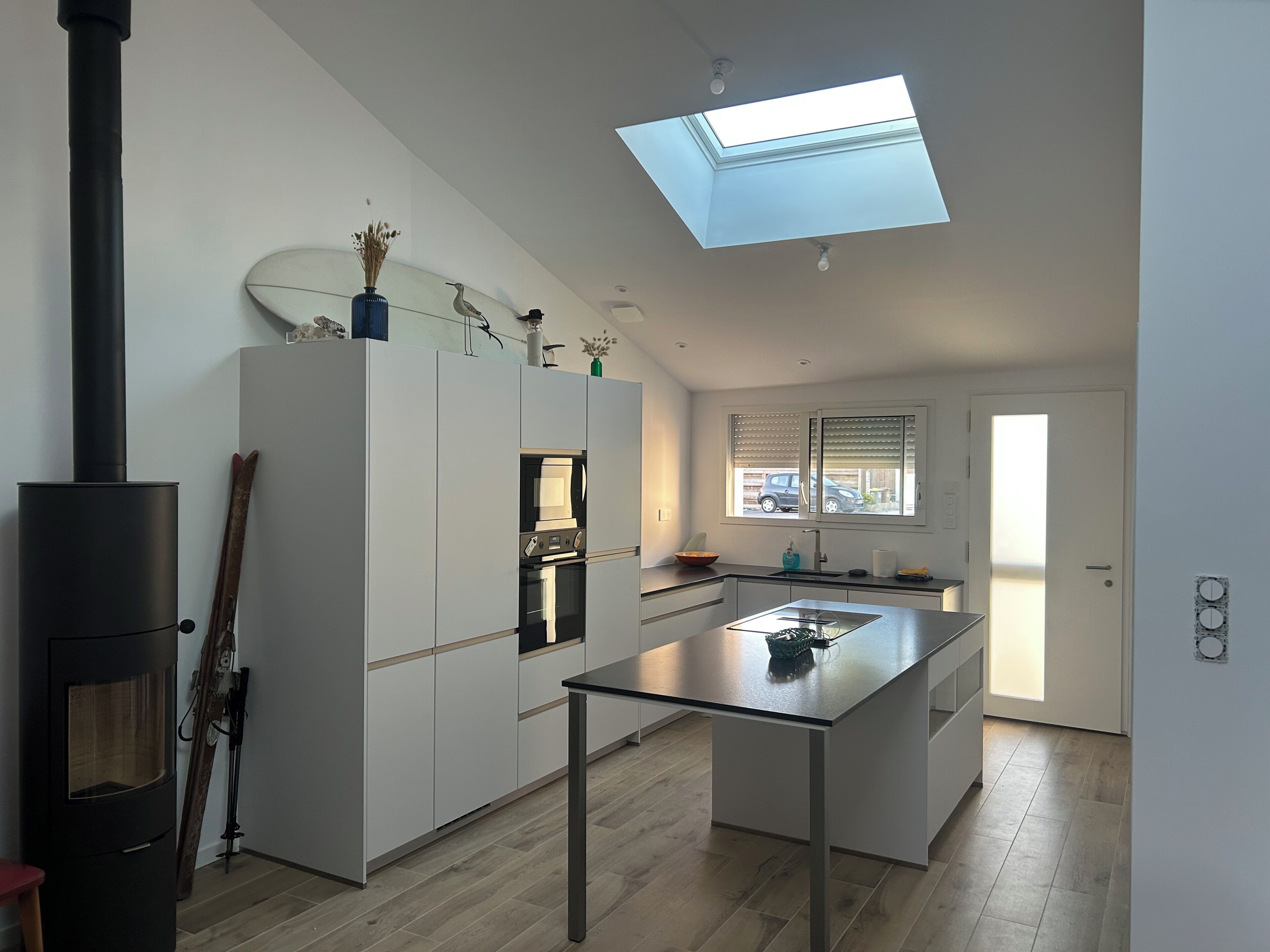 A modern kitchen with a central island, a built-in oven, and a skylight above.