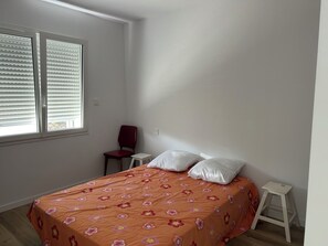 A bedroom with a bed, a chair, a small table, and a window with blinds. - House for rent near Les Conches Beach (700 m) (Longeville-sur-Mer)