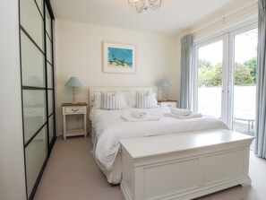 A bedroom with a large bed, bedside tables, a nightstand, a painting, and a view of the outdoors. - Machroes Cottage (Pwllheli)