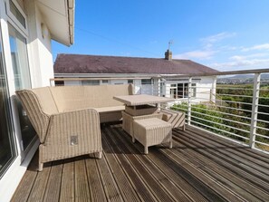 A wooden deck with wicker furniture, including a sofa and chairs, overlooking a residential area. - Machroes Cottage (Pwllheli)