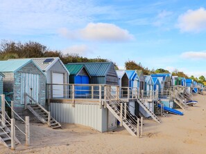 A row of beach huts with wooden staircases leading to the beach. - Machroes Cottage (Pwllheli)