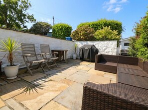 An outdoor patio with stone flooring, wicker furniture, and a barbecue grill. - Machroes Cottage (Pwllheli)