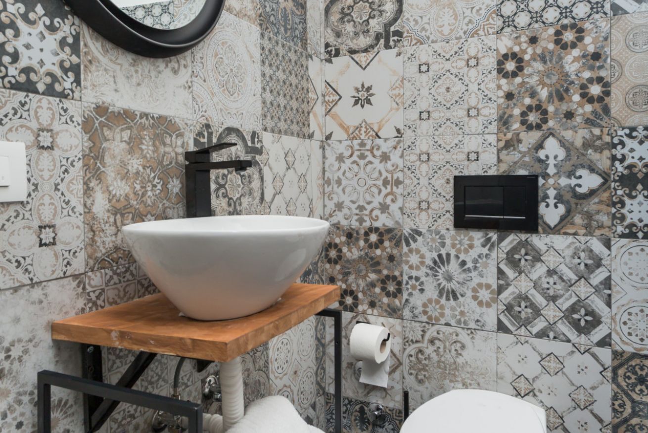 Une salle de bain avec un grand lavabo blanc posé sur une étagère en bois, un robinet noir et des carreaux décoratifs sur les murs.