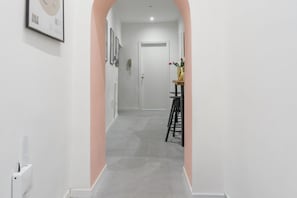 En hall med en vit dörr längst in, ett litet bord med en vas med blommor och en inramad tavla på väggen.