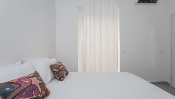 Hotellihuone, jossa on sänky, valkoiset verhot ja ikkuna.