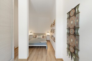 Un corridoio stretto conduce a una camera da letto con un letto, comodini e una mensola a parete con libri.