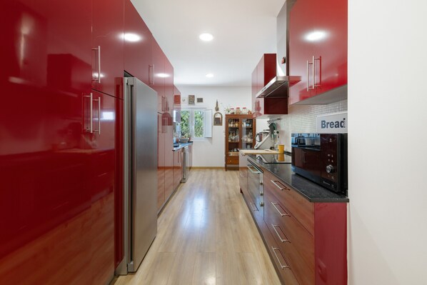A modern kitchen with red cabinetry, stainless steel appliances, and a wooden floor.