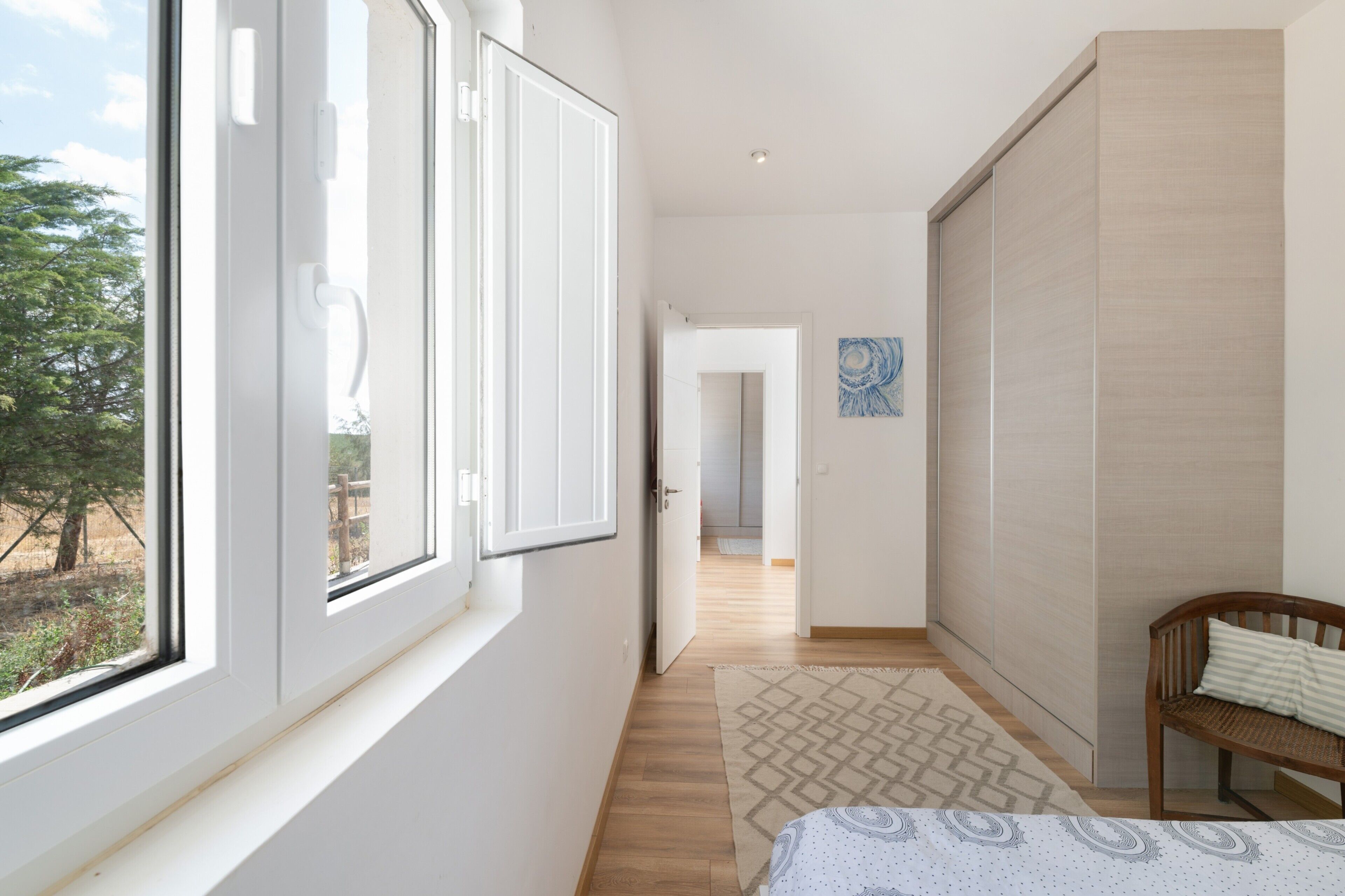 A hallway with a bed, a wooden bench, a patterned rug, and a painting on the wall.
