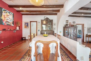 Zona pranzo con un tavolo grande, sedie e una parete rossa con un quadro.