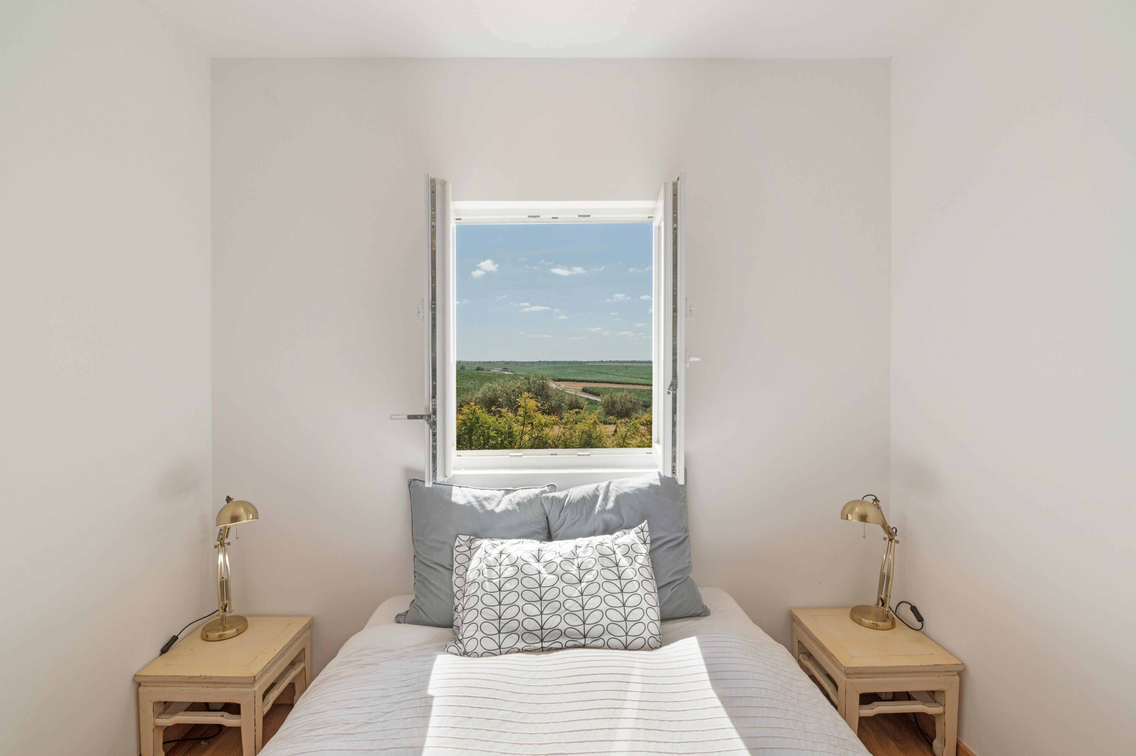 Quarto com uma janela grande, duas mesas de cabeceira e uma cama com almofada estampada.