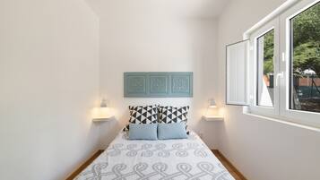 A bedroom with a bed, two bedside lamps, a window, and a wall-mounted decorative panel.