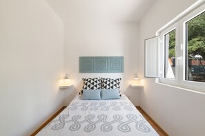 A bedroom with a bed, two bedside lamps, a window, and a wall-mounted decorative panel.