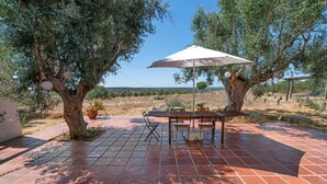 An outdoor patio with a table and chairs, surrounded by olive trees and a clear view of the landscape. - 'Excelentíssimo' Holiday Home with Lake View, Wi-Fi, and Air Conditioning (Torrão)