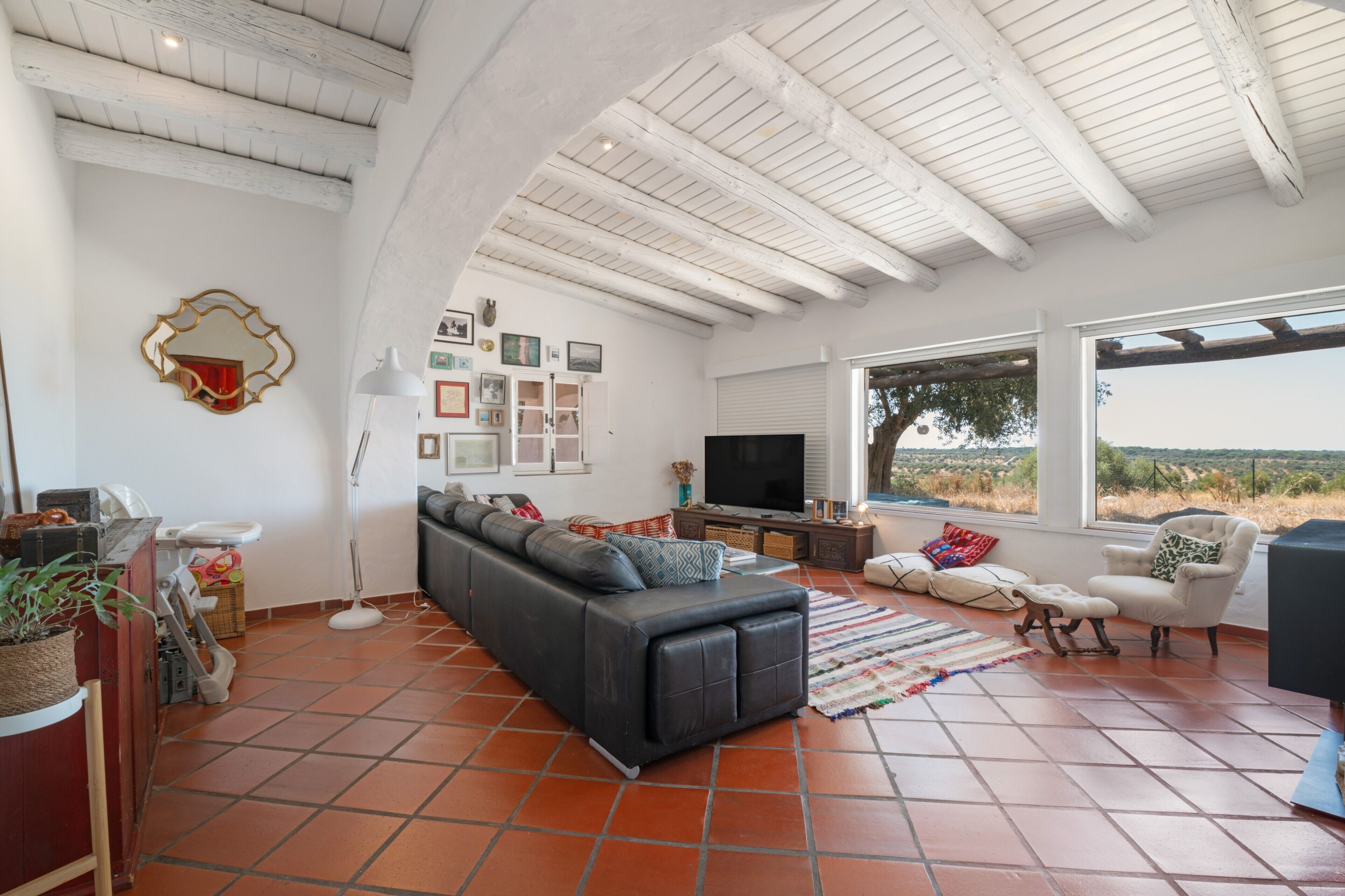 Un salón amplio con un sofá negro, un televisor y un ventanal con vistas al exterior.