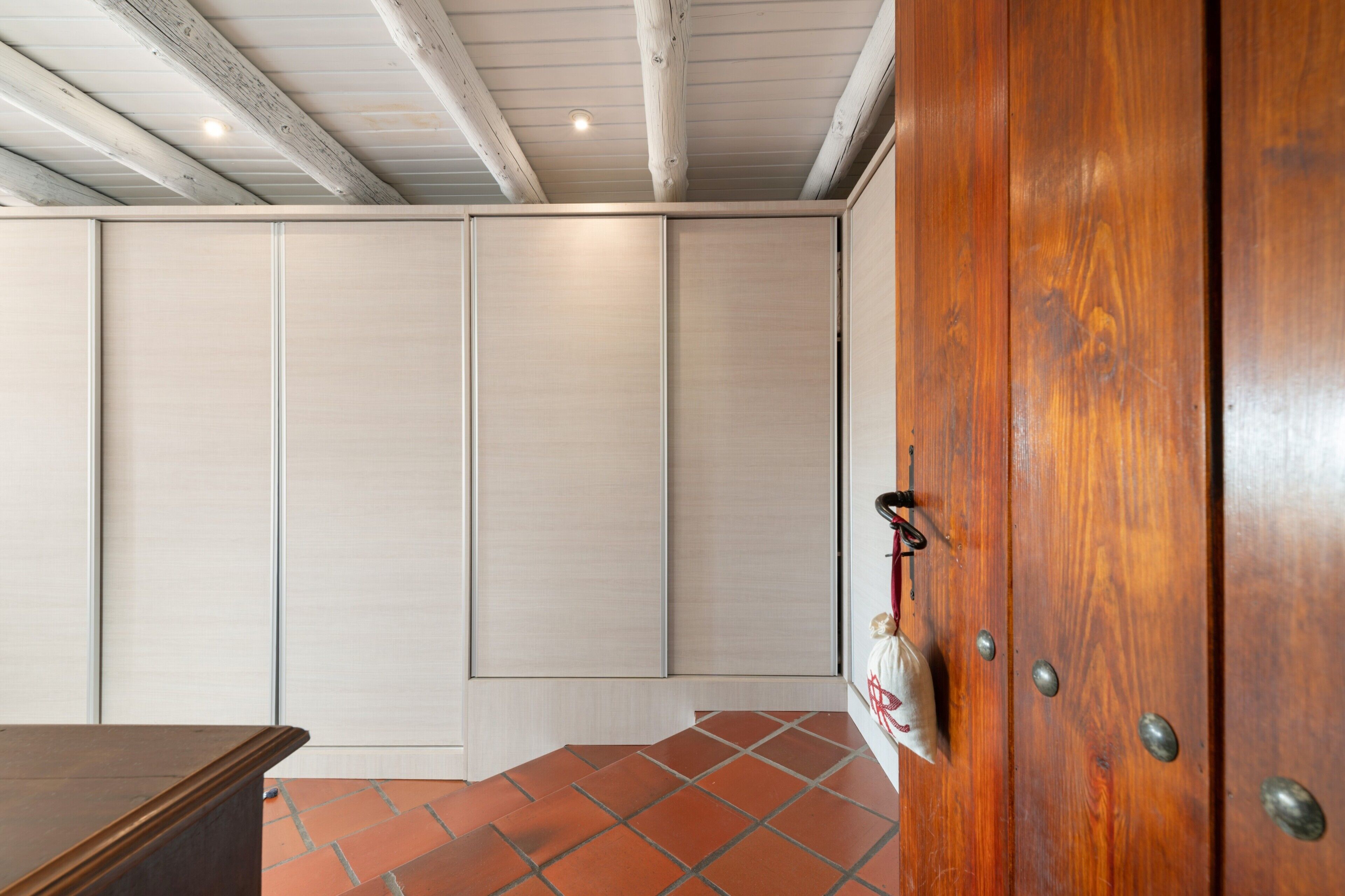 A room with a wooden door, a tiled floor, and a white wall with a sliding door.