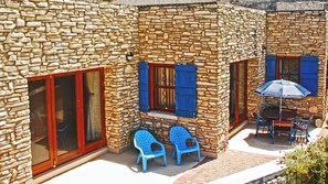 Edificio de piedra con un patio que incluye dos sillas de plástico azules, una mesa y una sombrilla.
