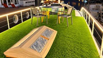 Un espace extérieur aménagé avec une table et des chaises sur une terrasse en bois, donnant sur une marina où sont amarrés des bateaux.