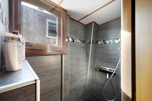 Et badeværelse med bruser, et vindue og en hylde med toiletartikler.