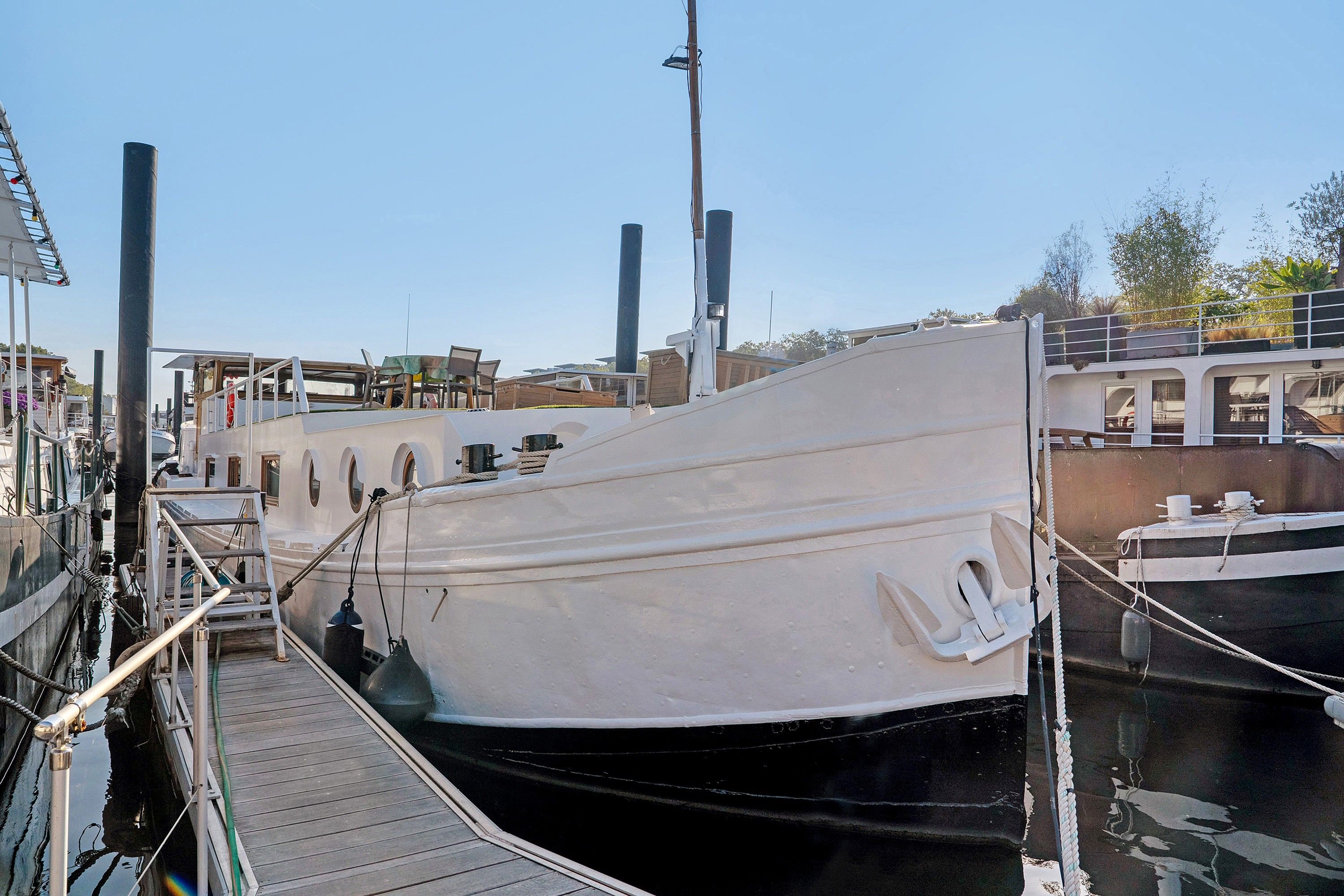 Una barca bianca ormeggiata in una marina, con una passerella in legno che vi conduce.