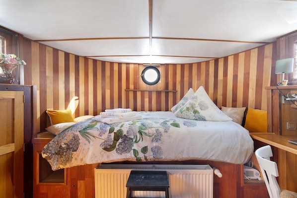 A bedroom with a bed, a round mirror, a desk with a lamp, and a chair.