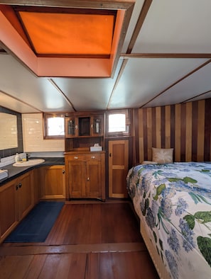 A compact interior with a wooden cabinet, a bed with floral bedding, and a small window.