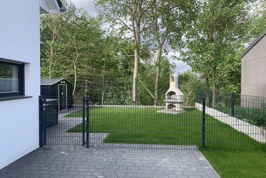 Un patio cercado con un sendero empedrado, una pequeña construcción y árboles.