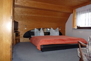 A bedroom with a bed, a chair, a television, and a window with curtains. - Holiday apartment with 2 bedrooms (Hohnstein)