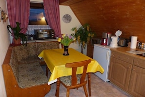 A cozy dining area with a table set for two, a wooden bench, and a small kitchenette with a refrigerator and coffee maker. - Holiday apartment with 2 bedrooms (Hohnstein)