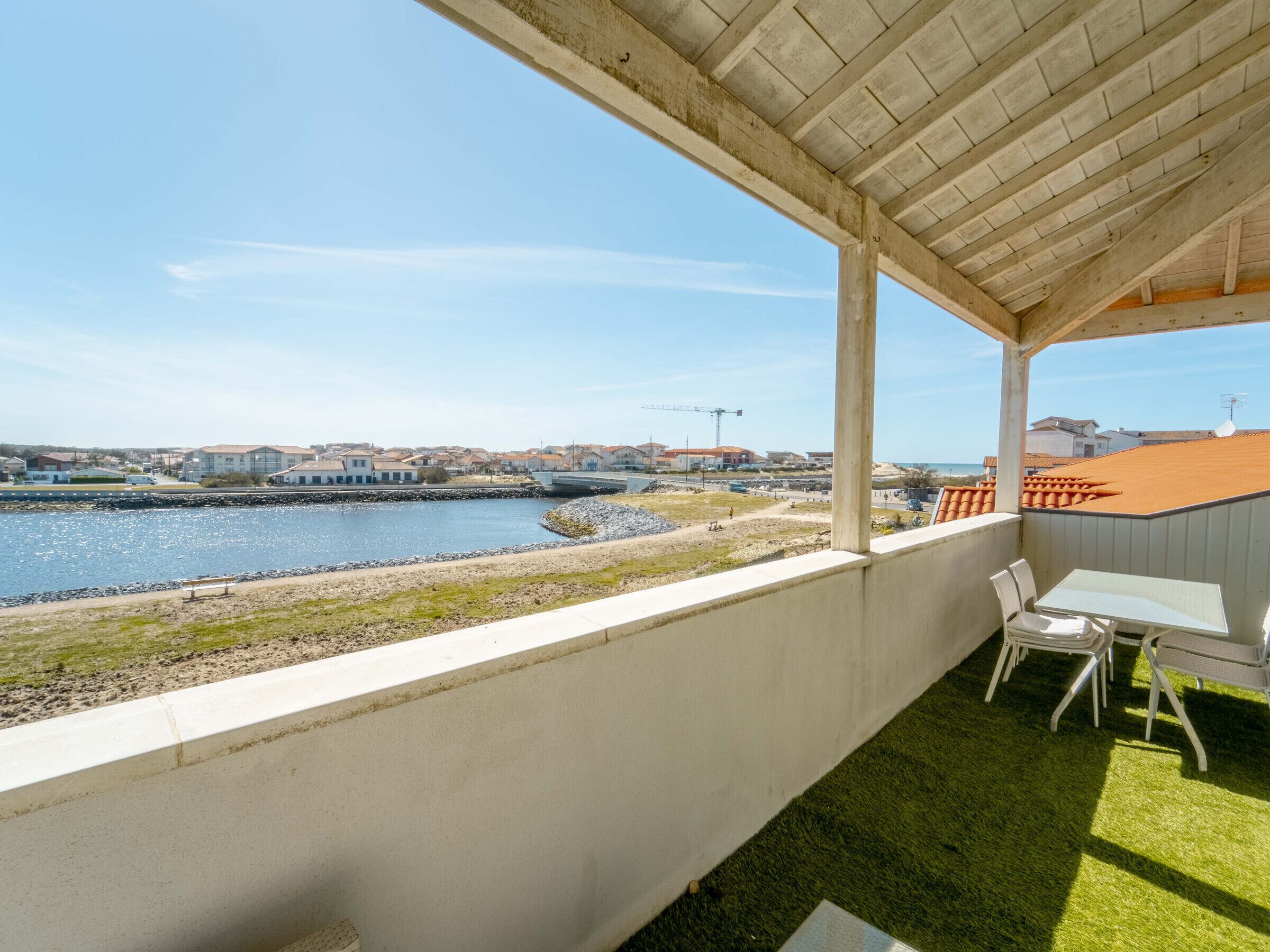 A balcony with a view of a river, a grassy area, and a row of buildings in the distance.