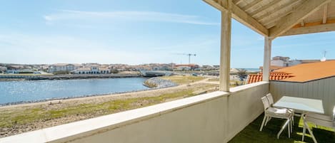 A balcony with a view of a river, a grassy area, and a row of buildings in the distance.