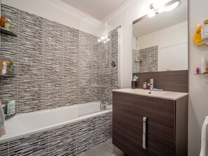 Ein modernes Badezimmer mit einer Wandgestaltung aus Holzlamellen, einer freistehenden Badewanne und einem dunkelholzfarbenen Waschtisch mit Spiegel.