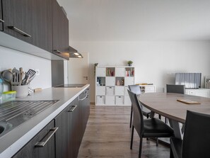 Eine moderne Küche mit Einbauherd, einem Essbereich mit rundem Tisch und Stühlen sowie einem weißen Bücherregal mit Büchern und Dekoration.