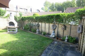 Ein Garten mit einer Steinterrasse, einem Grill und einem Holzzaun mit Zierfiguren.