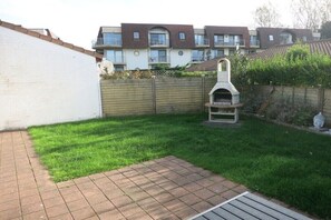 A backyard with a brick patio, a barbecue grill, and a wooden fence. - Holiday apartment with 2 bedrooms (Bredene)