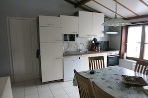 A compact kitchen with white cabinets, a microwave, a coffee maker, and a dining table with chairs.