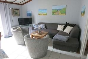 A living room with a sofa, two armchairs, a coffee table, and a flat-screen TV.