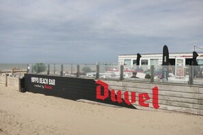 A beach bar named 'Hippo Beach Bar' with a large red logo and a sign indicating it's 'touched by Duvel.'