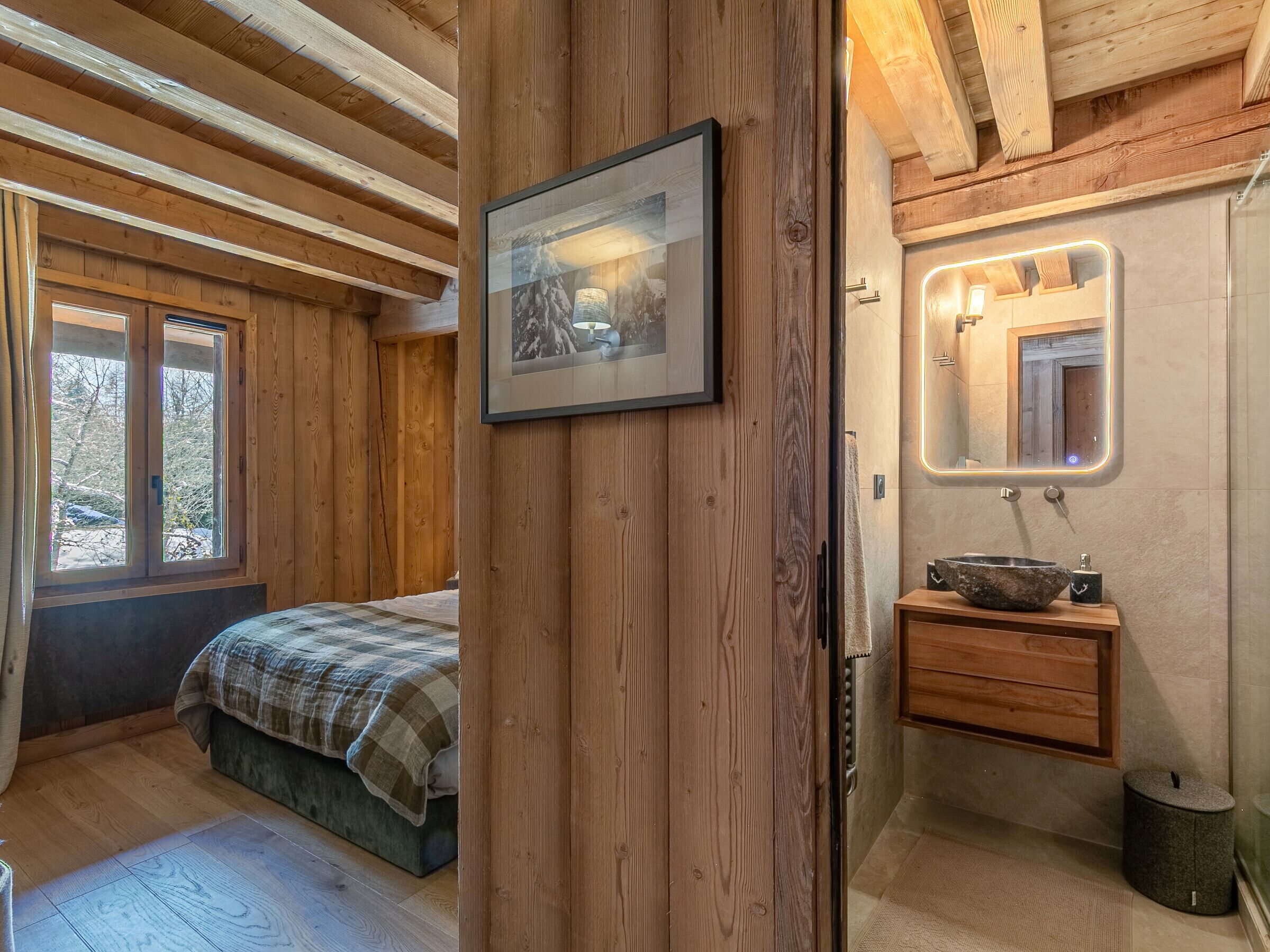 L’intérieur d’une cabane en bois comprend un lit, un tableau encadré, une salle de bain avec un miroir et un lavabo.
