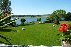 Ein gepflegter Rasen mit Blick auf einen See und Boote, umgeben von ordentlich geschnittenen Hecken und einigen Stühlen.