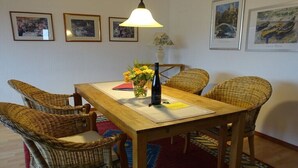 Spiseområde med et træbord, fletstole, en vase med blomster og billeder i rammer på væggen.
