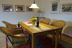 Un comedor con una mesa de madera, sillas de mimbre, un florero con flores y cuadros en la pared.