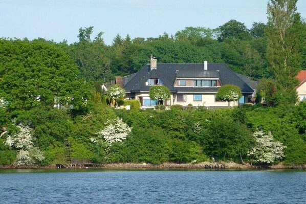 Una casa con un jardín amplio, un muelle y una masa de agua al frente.