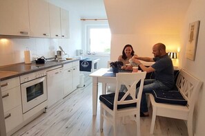 Eine moderne Küche mit weißen Schränken, eine Essecke mit weißem Tisch und Stühlen sowie ein Fenster, das für natürliches Licht sorgt.