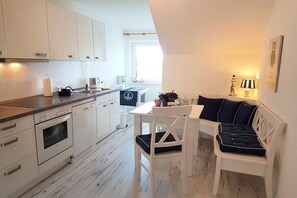 Une cuisine moderne avec des meubles blancs, un coin repas doté d’une table et de chaises blanches, et une vue sur l’extérieur.