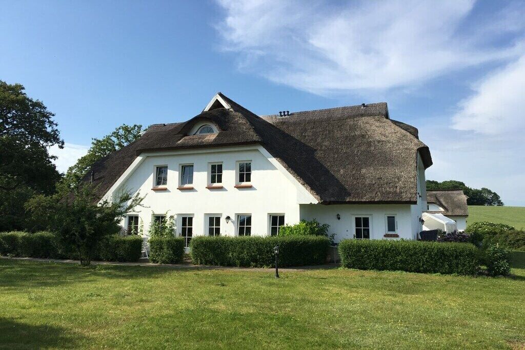 Een groot wit gebouw met een steil dak, omgeven door een verzorgd gazon en heggen.